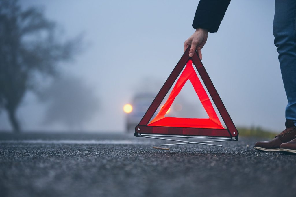 A hand is dropping a Warning triangle on the road
